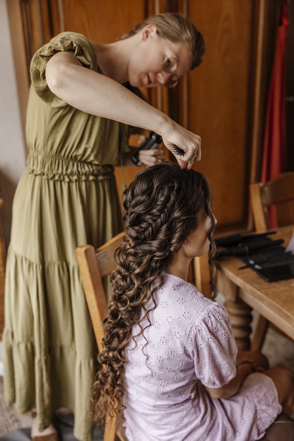 Johanna vlecht het haar van een vrouw in een lila jurk